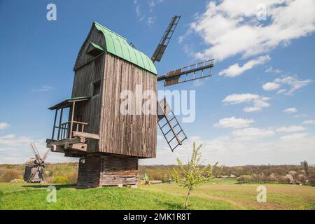 Antike Holzwindmühlen auf einem Hügel in der Nähe des Dorfes. Ländliche Landschaft Stockfoto