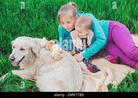 Zwei Schwestern sehen Hühner an, die im Garten auf einem weißen Hund sitzen Stockfoto