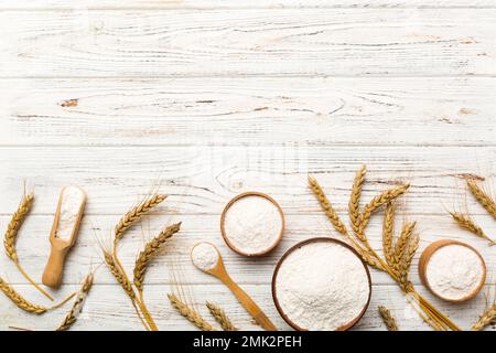 Flaches Lay Weizenmehl in Holzschale mit Weizenspikelets auf farbigem Hintergrund. Weltweizenkrise. Stockfoto