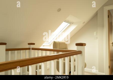 Flacher Fokus eines Lichtschalters, der am Ausgang zum Schlafzimmer zu sehen ist. Ein großer Flur im ersten Stock mit Dachfenstern ist zu sehen. Stockfoto