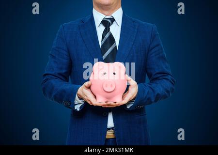 Ein Geschäftsmann im Anzug hält Sparschwein. Geschäftsmann mit Schweinegeld Stockfoto