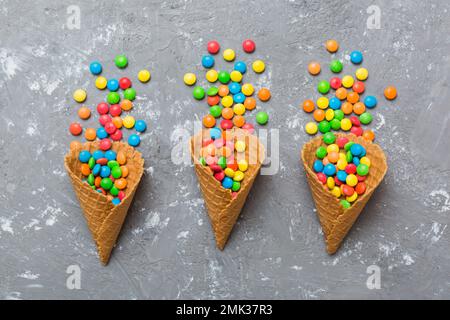 Waffelkonus voller traditioneller Süßigkeiten, die auf farbigen Hintergrund fallen, mit Platz für Kopien. Frohes Weihnachtsangebot. Stockfoto