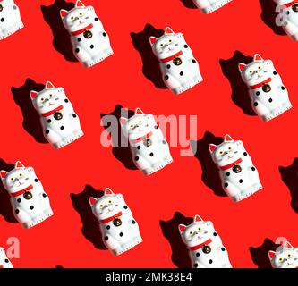 Nahtloses Muster von Maneki-Neko-Katzen auf rotem Hintergrund. Winkende Katze. Die rechte Pfote der Glückskatze ist angehoben. Stockfoto