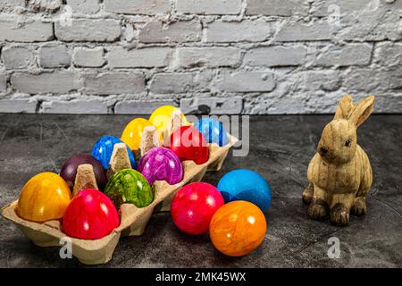 Eierkarton mit bunten ostereiern und osterhasen vor der weißen Backsteinwand Stockfoto