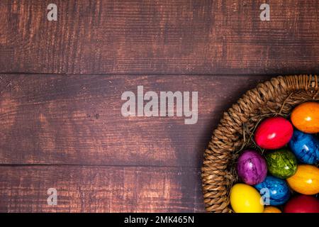 Runder osterkorb mit bunten ostereiern auf rustikalem weißen Holztisch Stockfoto