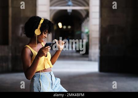 Frau tanzt, während sie mit Mobiltelefon und Kopfhörern im Freien Musik hört. Stockfoto
