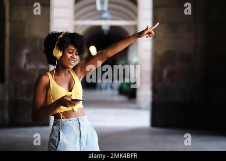 Frau mit geschlossenen Augen tanzt entspannt und hört Musik mit Kopfhörern im Freien. Stockfoto