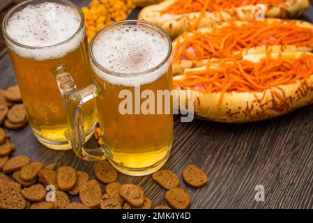 Zwei Gläser Bier, Hot Dogs und Snacks für Bier auf einem Holztisch Stockfoto