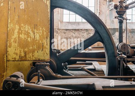 Fragment des Dampfgenerators für Dampfmotoren in historischen Fabriken aus dem Jahre 1903. Riesiges Schwungrad und gelbes Gehäuse der Maschine. Rostwand in t Stockfoto