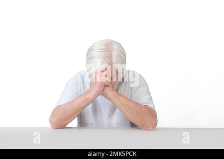 Horizontale Aufnahme eines alten Mannes, dessen Ellbogen sich auf einem Tischkopf verbeugt im Gebet. Isoliert auf weiß. Viel Platz zum Kopieren. Stockfoto