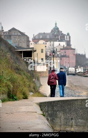 Ein Paar mittleren Alters, das Arm in Arm am Ufer von cromer norfolk england entlang spaziert Stockfoto