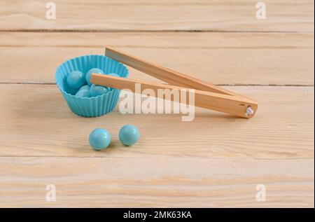 Pinzette zum Greifen von Kugeln mit blauen Kugeln auf Holzhintergrund. Montessori, die Entwicklung des Geistes von Kindern Stockfoto