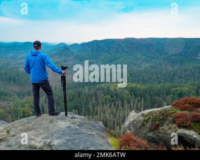 Fotograf mit gefaltetem Stativ am Ende des Klippendenkens. Natürliche Waldlandschaft im wunderschönen Tal Stockfoto