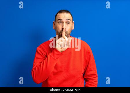 Ein seriöser gutaussehender, bärtiger hispano-Mann hält sich den Zeigefinger an die Lippen, versucht, die Verschwörung zu halten, schaut beiseite und sagt: "Psst, sei bitte still. Stockfoto