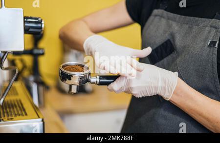 Seitlicher Barista mit Latexhandschuhen für die Zubereitung der Kaffeemaschine. Hochauflösendes Foto Stockfoto