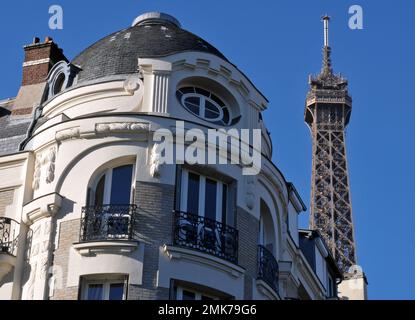 Der Gipfel des berühmten Eiffelturms erhebt sich hinter einem prunkvollen Wohngebäude in Paris. Stockfoto