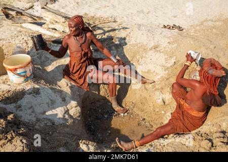Himba-Frauen sammeln Wasser an einem Wasserloch, am Ufer des trockenen Flussbettes des Hoarusib, Kaokoland, Kunene Region, Namibia Stockfoto