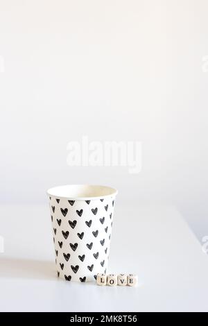 Das Wort "Liebe" besteht aus Holzwürfeln und einem Papierglas mit schwarzen Herzen, isoliert auf weißem Hintergrund Stockfoto