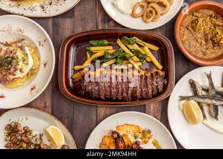 Auswahl an Gerichten und Tapas der spanischen Gastronomie mit Scheiben gegrilltem Rindfleisch mit pommes Frites, galizischem Tintenfisch, gebratenen Sardellen, gebratener Calamari, Stockfoto