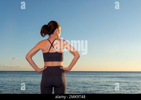 Fit für Damen mit Händen an der Hüfte und Blick auf das Meer in Sportbekleidung. Entspannung nach dem Training. Stockfoto