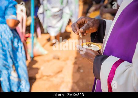 Nahaufnahme der Hände eines afrikanischen Priesters, der das sakramentale Brot den Gläubigen geben wird Stockfoto