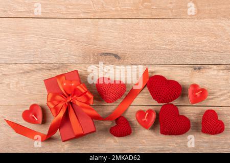 Rote Geschenkbox mit gestrickten roten Herzen und mit roten Kerzen in Herzform auf Holzhintergrund. Alles gute zum Valentinstag, Muttertag und bir Stockfoto