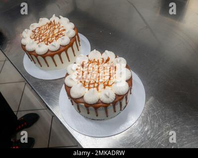 Der Bäcker bereitet salzige, karamellbeschichtete, tropfende weiße Kuchen mit Baiser zu Stockfoto