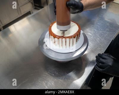 Der Bäcker bereitet salzige, karamellbeschichtete, tropfende weiße Kuchen mit Baiser zu Stockfoto