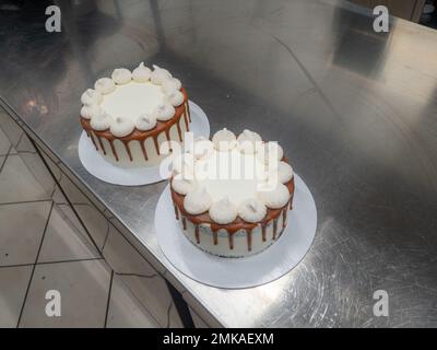 Der Bäcker bereitet salzige, karamellbeschichtete, tropfende weiße Kuchen mit Baiser zu Stockfoto