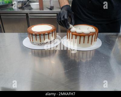 Der Bäcker bereitet salzige, karamellbeschichtete, tropfende weiße Kuchen mit Baiser zu Stockfoto