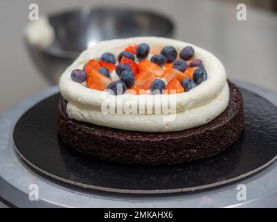 Der Chefkoch, der Gebäck designt, konfektioniert einen mit Erdbeeren, Blaubeeren und Schlagsahne gefüllten Kuchen im 3. Stock. Kuchenstruktur bef Stockfoto