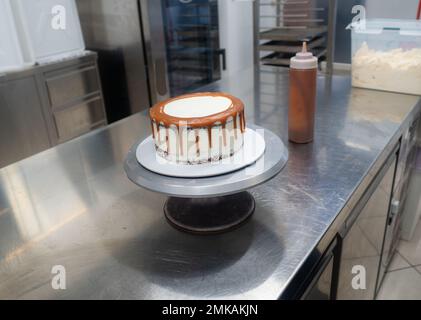 Der Bäcker bereitet salzige, karamellbeschichtete, tropfende weiße Kuchen mit Baiser zu Stockfoto