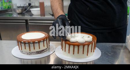 Der Bäcker bereitet salzige, karamellbeschichtete, tropfende weiße Kuchen mit Baiser zu Stockfoto