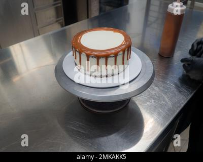 Der Bäcker bereitet salzige, karamellbeschichtete, tropfende weiße Kuchen mit Baiser zu Stockfoto