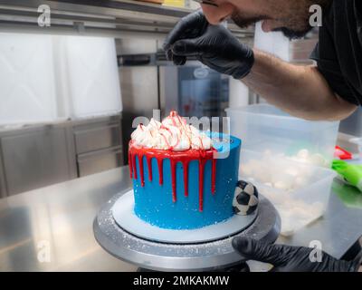 Blau besprühter, mattierter Kuchen auf dem Ständer, mit roter Ganache Füllung und weißen Baiser und Schlagsahne oben drauf Stockfoto