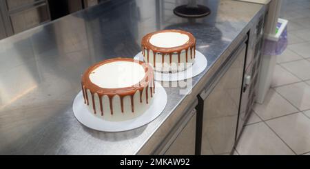 Der Bäcker bereitet salzige, karamellbeschichtete, tropfende weiße Kuchen mit Baiser zu Stockfoto