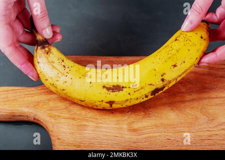 Reife gelbe Banane auf dem Schneidebrett. Banane in Frauenhänden. Stockfoto