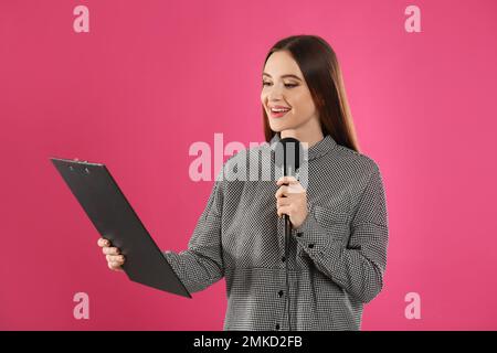 Junge Journalistin mit Mikrofon und Klemmbrett auf pinkfarbenem Hintergrund Stockfoto