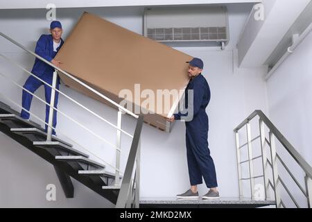 Professionelle Arbeiter, die Kühlschränke auf Treppen in Gebäuden tragen Stockfoto
