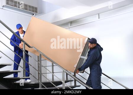 Professionelle Arbeiter, die Kühlschränke auf Treppen in Gebäuden tragen Stockfoto