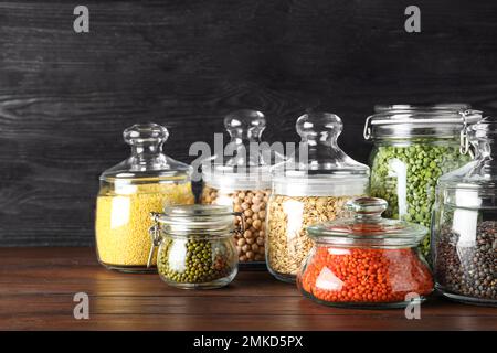 Verschiedene Arten von Hülsenfrüchten und Getreide in Glasgefäßen auf Holztisch. Organische Körner Stockfoto