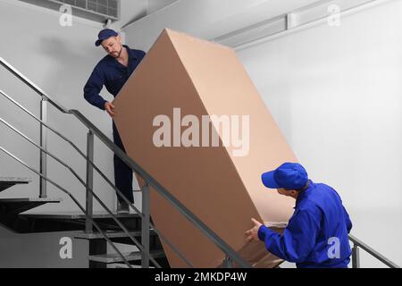 Professionelle Arbeiter, die Kühlschränke auf Treppen in Gebäuden tragen Stockfoto