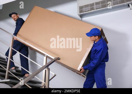 Professionelle Arbeiter, die Kühlschränke auf Treppen in Gebäuden tragen Stockfoto
