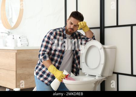 Junger Mann fühlt sich angewidert, als er die Toilettenschüssel im Bad reinigte Stockfoto