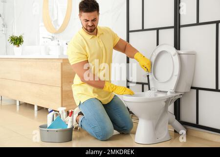 Junger Mann fühlt sich angewidert, als er die Toilettenschüssel im Bad reinigte Stockfoto