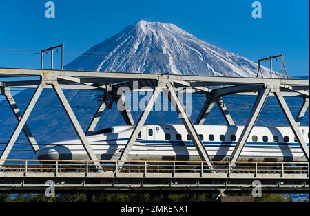 Ein Zug der JR Central N700 der Tokaido Shinkansen Line überquert eine Brücke über den Fuji River (Fujikawa), wobei der Fuji in der Präfektur Shizuoka zu sehen ist. Stockfoto