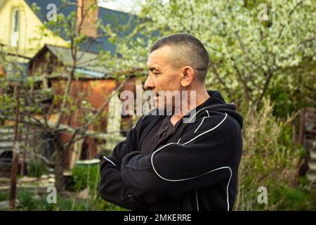 Pflanzen von Gemüse unter dem handgeführten Traktor. Ein Mann mit einem begehbaren Traktor im Garten. Manuelles Arbeiten mit Geräten. Ein älterer Mann unterrichtet Stockfoto