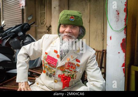 Ein älterer vietnamesischer Militärveteran zeigt stolz seine Kriegsmedaillen, während er in einer Straße im Zentrum von Hanoi, Vietnam, sitzt. Stockfoto