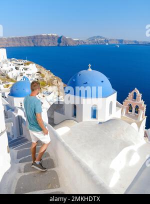 Junge Männer Touristen besuchen Oia Santorini Griechenland an einem sonnigen Tag im Sommer mit weißen Häusern und Kirchen, griechische Insel Ägäische Kykladen Stockfoto