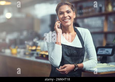 Es war noch nie so einfach, mit Kunden in Kontakt zu treten. Eine junge Frau, die ein Telefon in dem Laden benutzt, in dem sie arbeitet. Stockfoto